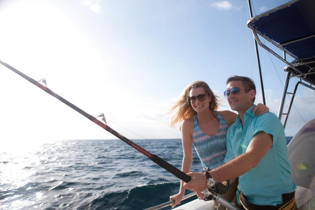 Pāris priecājās par zveju laivā, baudot saulainu dienu pie jūras. Viņi ir apģērbušies pludmales apģērbā un izskatās laimīgi.