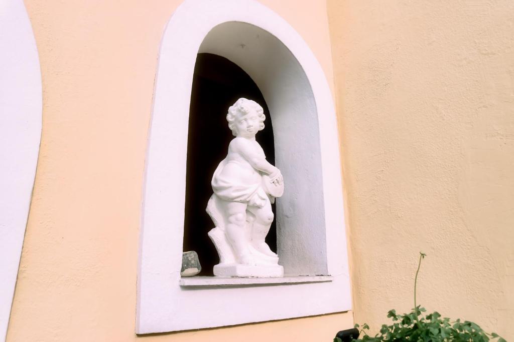 Balta statuja, kas attēlo bērnu, atrodas nišā pie dzeltenas sienas, radot šarmantu un mājīgu atmosfēru.