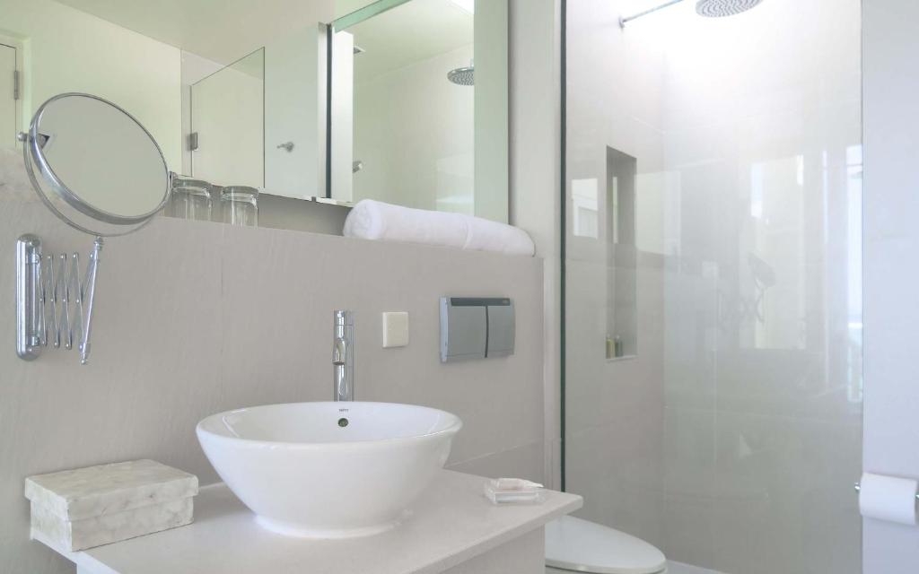 Mūsdienīgs un elegants vannas istabas interjers ar baltu izlietni, spoguli un dušas kabīni. Telpa ir gaiša un gaumīgi iekārtota.