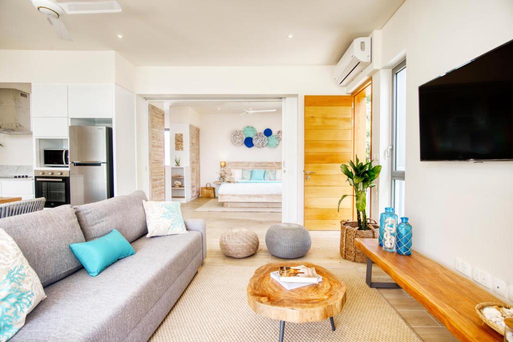 Mūsdienīgs un gaišs interjers ar ērtu dīvānu, koka galdu un modernu televizoru, radot viesmīlīgu atmosfēru. Telpā ir redzami dekoratīvi elementi un augi, kas piešķir dzīvīgumu.