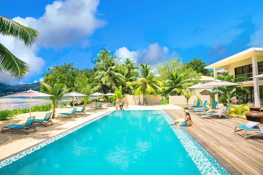 Peldbaseins ar palmām un sauļošanās krēsliem tropu pludmalē, ideāla vieta atpūtai un relaksācijai. Skaists laika apstākļs un zila debess papildina šo idillisko skatu.