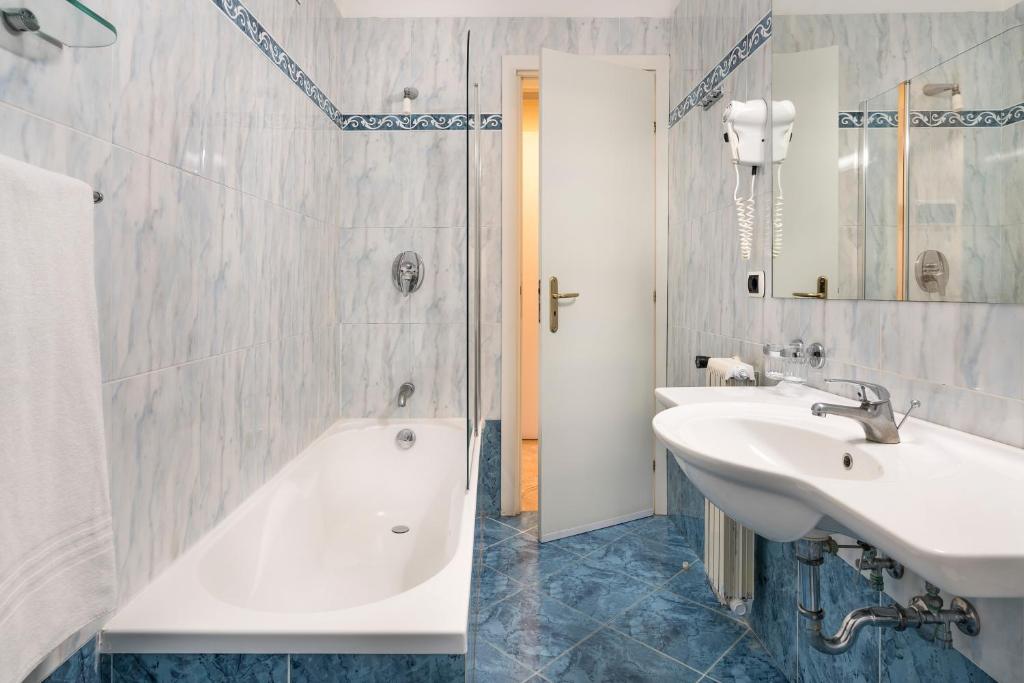 Mūsdienīgs vannas istabas interjers ar vannu un izlietni, baltiem flīzēm un zilām akcentu detaļām. Iekārtojums ir funkcionāls un estētisks.