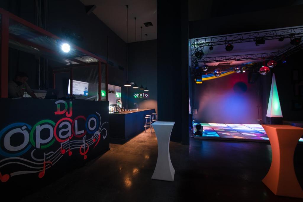 Mūzikas kluba interjers ar DJ pultu un gaismas efektu deju grīdu. Atmosfēra ir dinamiska un moderni iekārtota, ar krāsainiem apgaismojumiem un stilīgām mēbelēm.