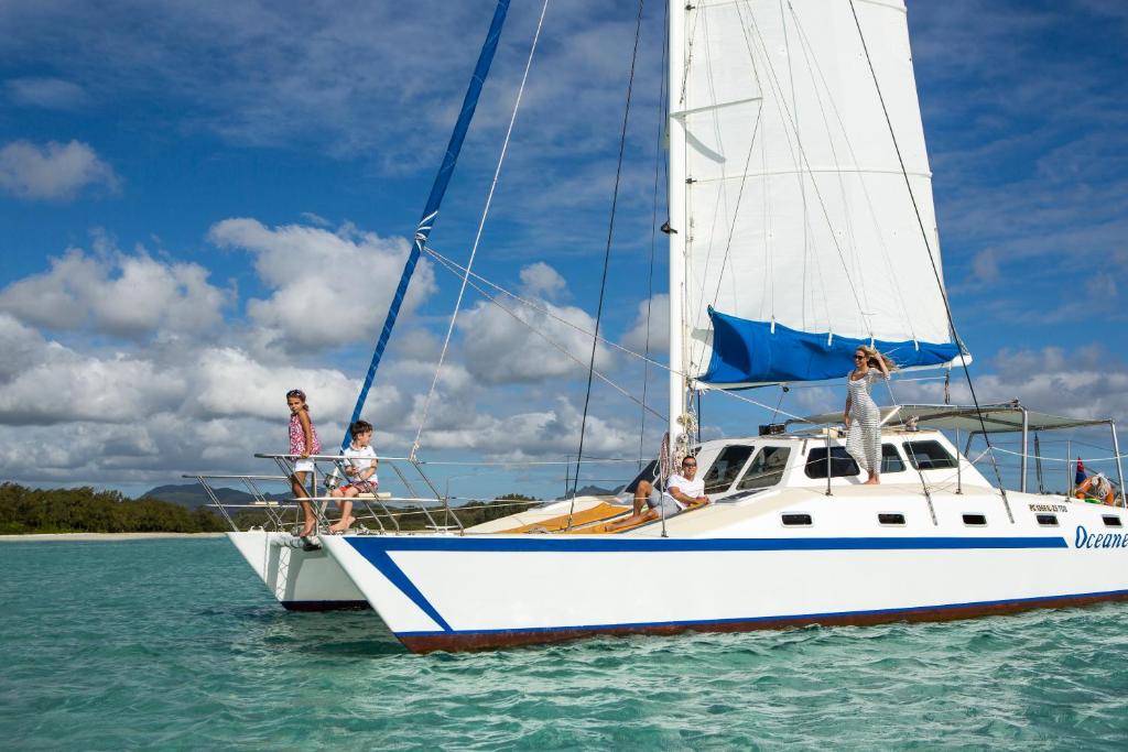 Jautra grupa cilvēku atpūšas uz jahtas, plūstošas ūdens virsmas, ar skaistu debess skatu un baltām mākoņu pūkām. Ideāls brīvdienu mirklis jūras vidē.