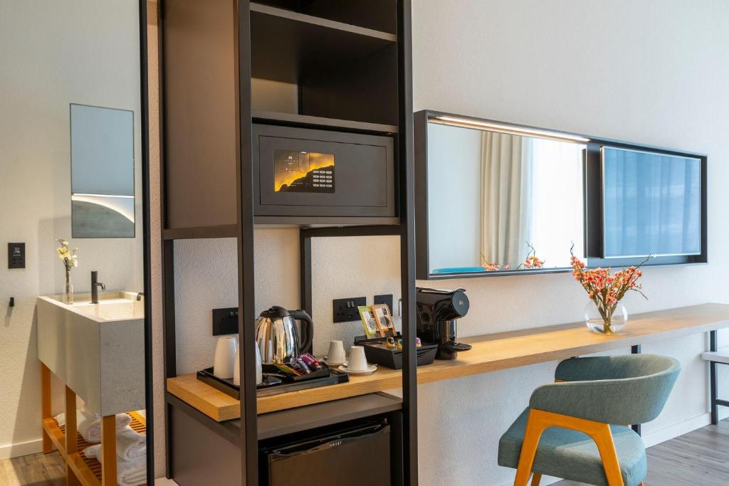 Mūsdienīgs viesnīcas numurs ar elegantu interjeru, kas ietver mikroviļņu krāsni, kafijas automātu un dekoratīvās ziedu kompozīcijas uz galda.