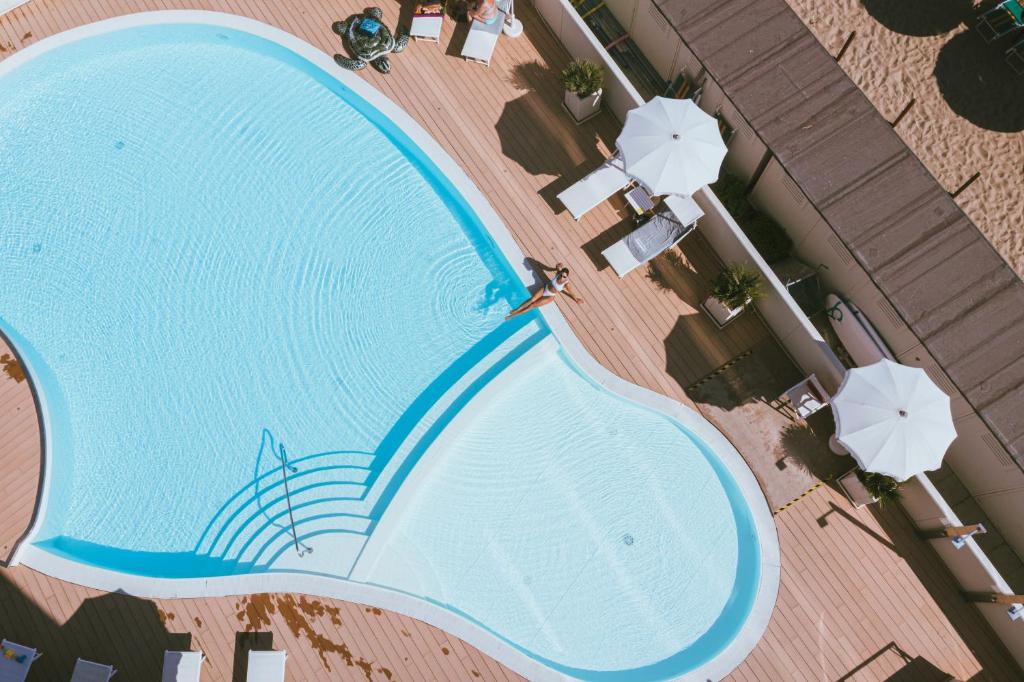 Baseins ar viļņojošu ūdeni un saulessargiem, izvietots uz koka terases, radot relaksējošu atmosfēru. Ideāla vieta atpūtai un izklaidei.