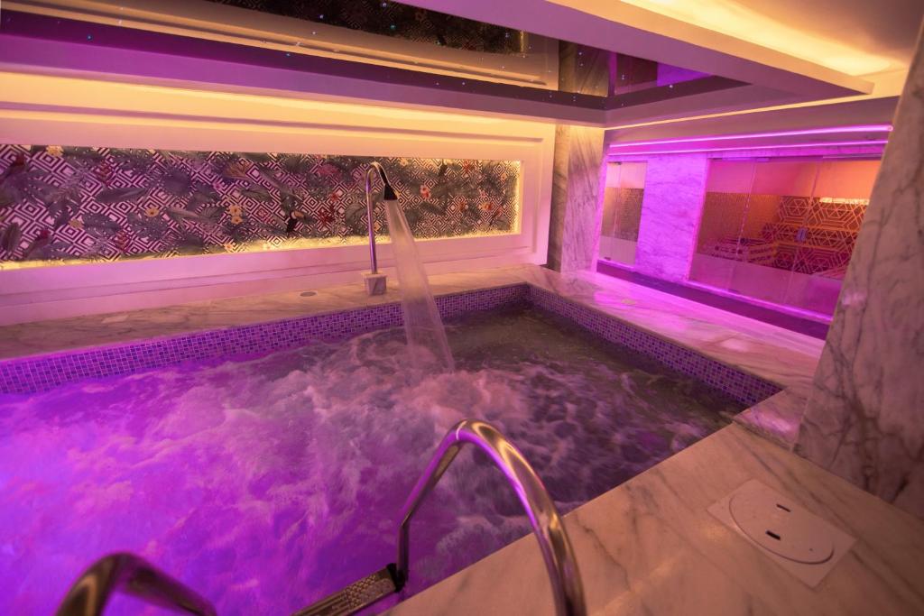Mūsdienīgs spa ar relaksējošu burbuļvannu, kas apgaismota ar rozā un violetām gaismām, radot nomierinošu atmosfēru. Marbles un stilīgas dekorācijas piešķir telpai elegantu izskatu.