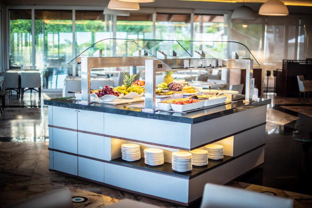Mūsdienīgs bufetes galdiņš ar augļiem un citiem ēdieniem, kas atrodas elegantā restorānā. Interjers ir gaišs un plašs, ar daudzām sēdvietām.