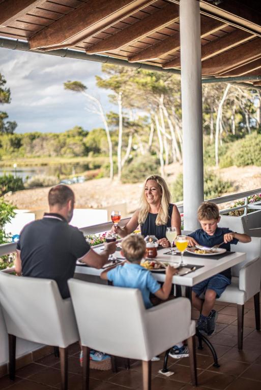 Ģimenes vakariņas restorānā ar bērniem, baudot ēdienu un dzērienus, skaistā dabas ainavā.