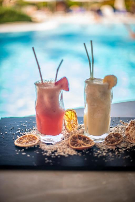 Divi kokteiļi ar augļu rotājumiem uz melna šķīvja, fonā peldbaseins. Ideāla vasaras atpūtas atmosfēra.