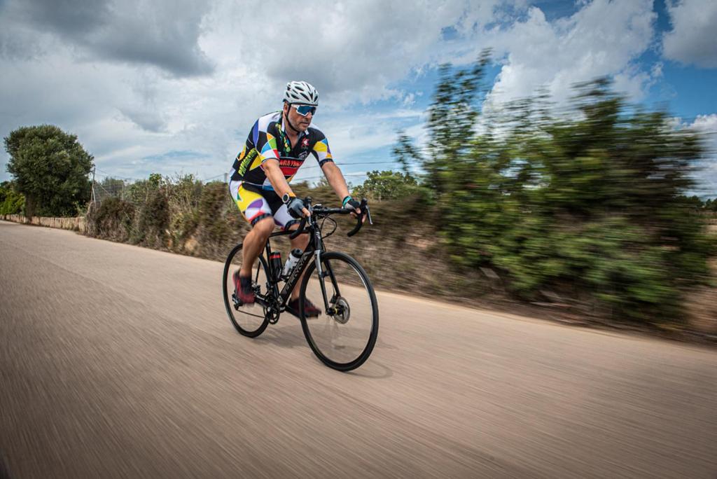Velo braucējs aktīvi pārvietojas pa ceļu ar ainavisku fonu un gaismas efektiem, kas rada kustības sajūtu.