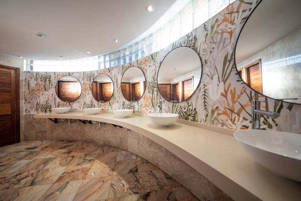 Moderns un elegants vannas istabas interjers ar apaļiem spoguļiem un stilizētu augu motīvu tapetēm. Vannas istabā ir plaša izlietne ar minimālistisku dizainu un dabīgā akmens grīda.