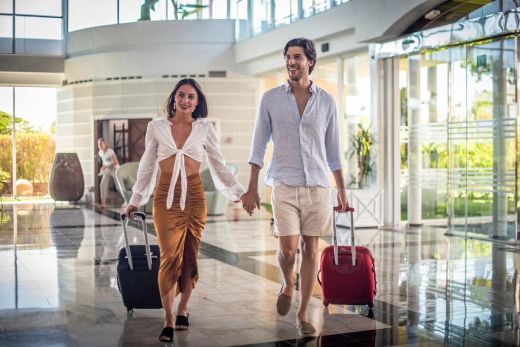 Jauni pāris, kas turas rokās, ienāk viesnīcā ar bagāžu, izskatoties laimīgi un relaksēti. Apspīdēts ar dabiskiem gaismas avotiem, interjers ir moderns un stilīgs.