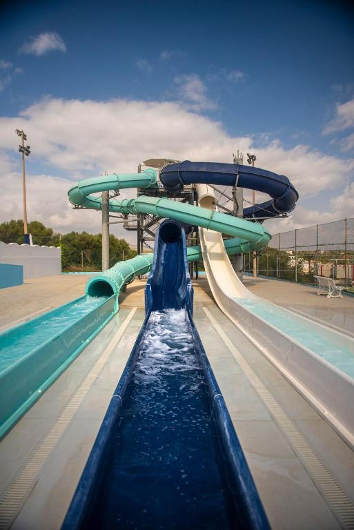 Ūdens slidkalniņu komplekss ar dažādām slidām, kas ved uz baseinu, zem zila debesu fona.