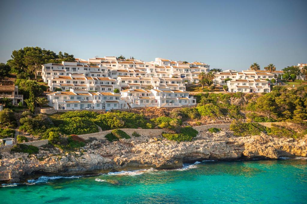 Balinātas viesnīcas un mājas, kas izvietotas piekrastes klintīs ar skatu uz zilajiem ūdeņiem. Apkārtne ir zaļa un saulaina, radot mierīgu atpūtas atmosfēru.