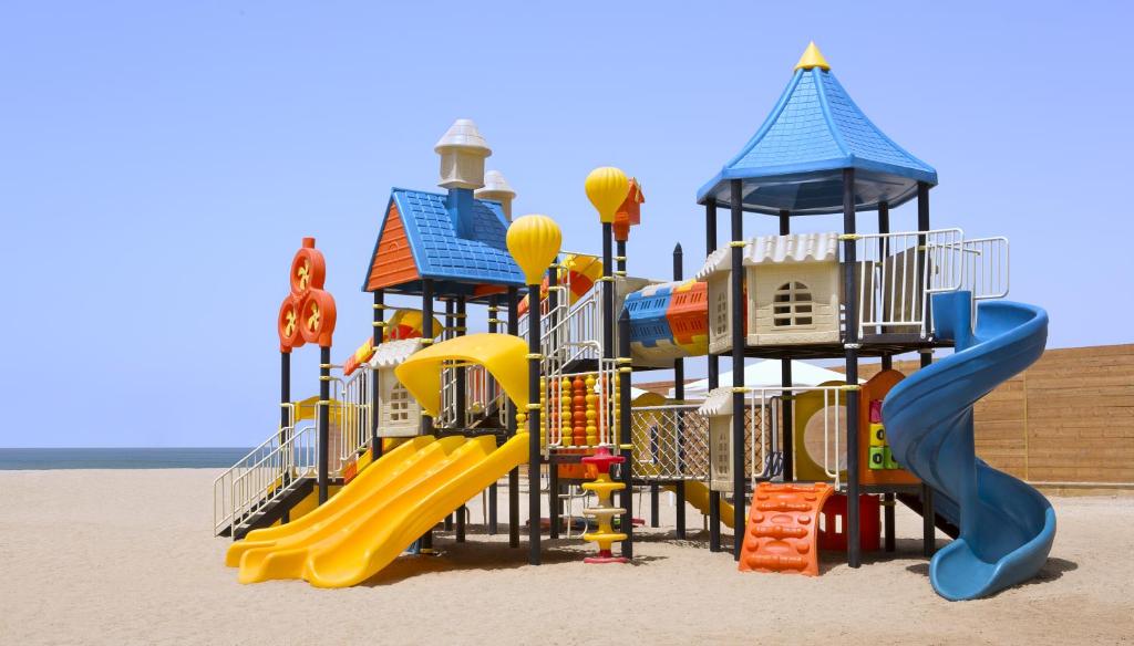 Krāsains bērnu rotaļu laukums ar slidkalniņiem un spēļu struktūrām, kas atrodas pludmalē. Ideāla vieta bērniem aktīvi pavadīt laiku ārā.