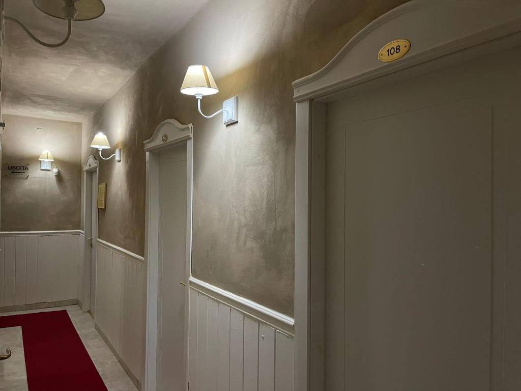 Gaismas koridors ar numuriem un sarkanu paklāju, apgaismots ar sienas lampām. Redzami numuri 108 un norāde "USCITA".