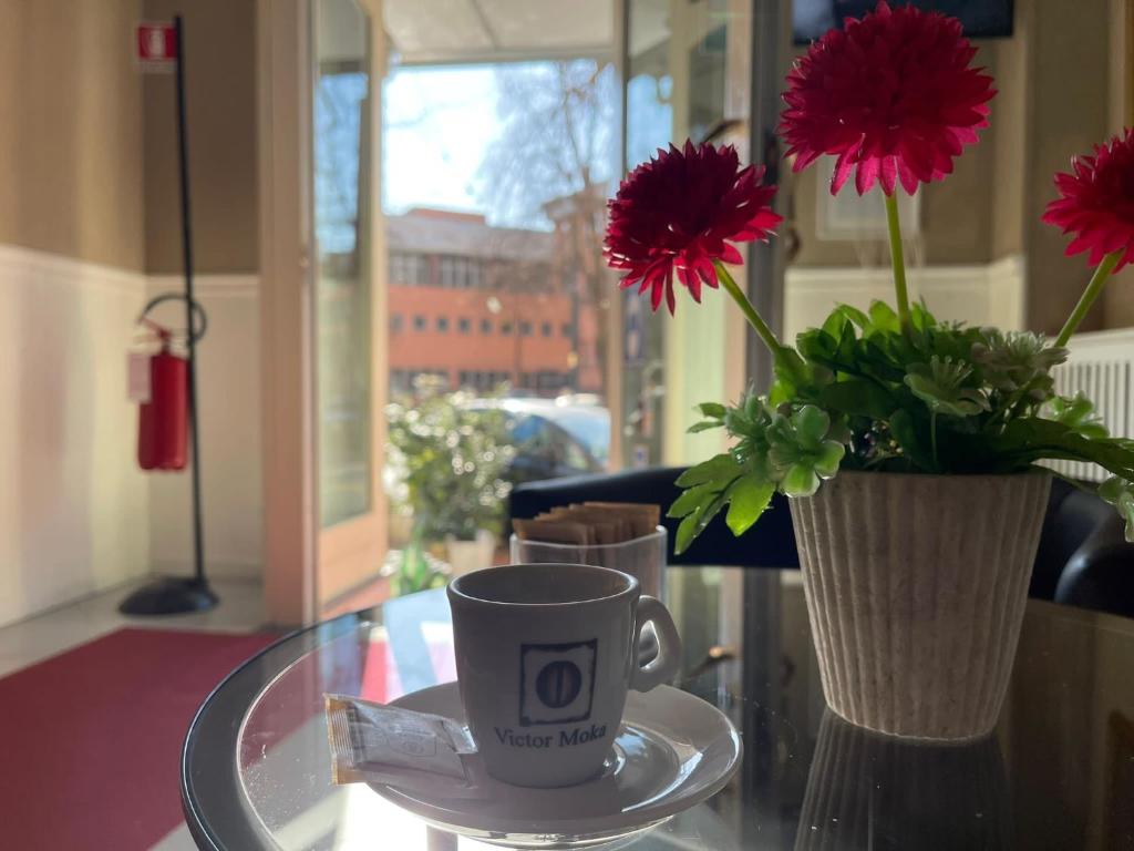 Kafijas krūze uz galda, blakus ziedu pušķis un gaiša iekārtojuma fons, kas rada mājīgu atmosfēru.