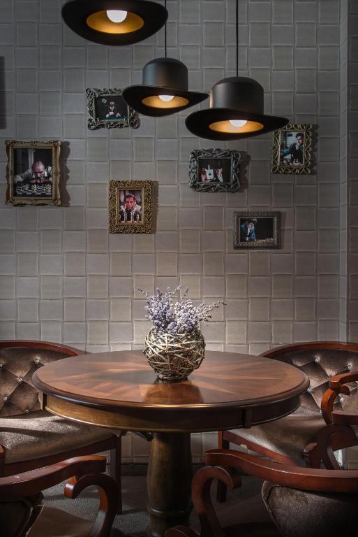 Koka galds ar ziedu kompozīciju centrā, ap kuru ir elegantas krēsli. Sienā atrodas melni rāmji ar fotogrāfijām un stilīgas lampas, kas rada mājīgu atmosfēru.