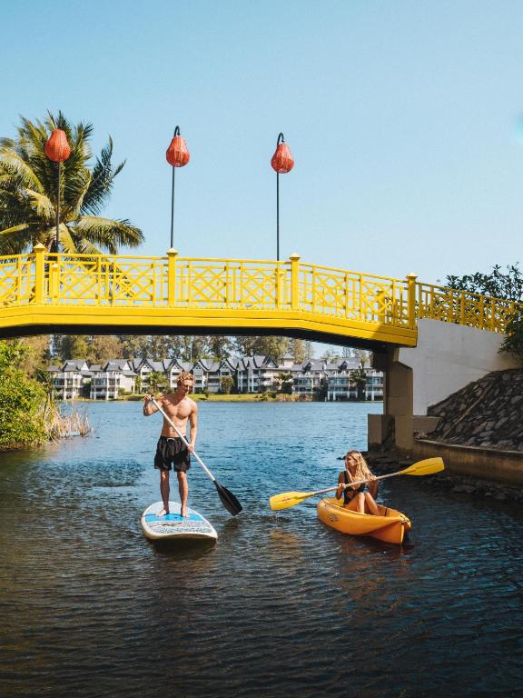 Pāris izbauda ūdenssportu pie Angsana Laguna Phuket, ar dzelteno tiltu fonā.