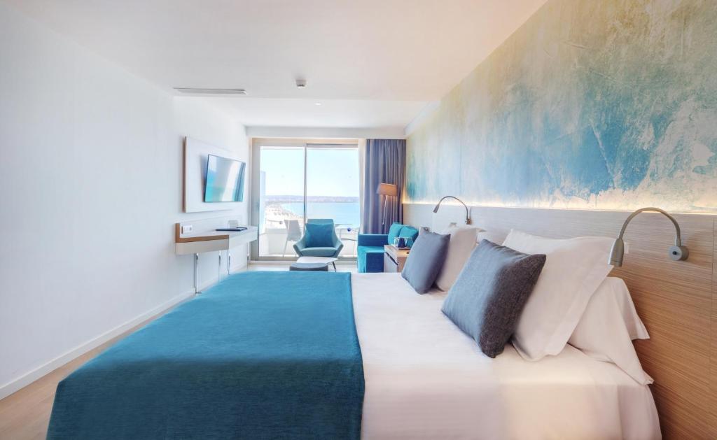 Moderns viesnīcas numurs ar skatu uz jūru, gaišām krāsām un komfortablu interjeru. Numurā atrodas liela gulta, televizors un sēdvietas.