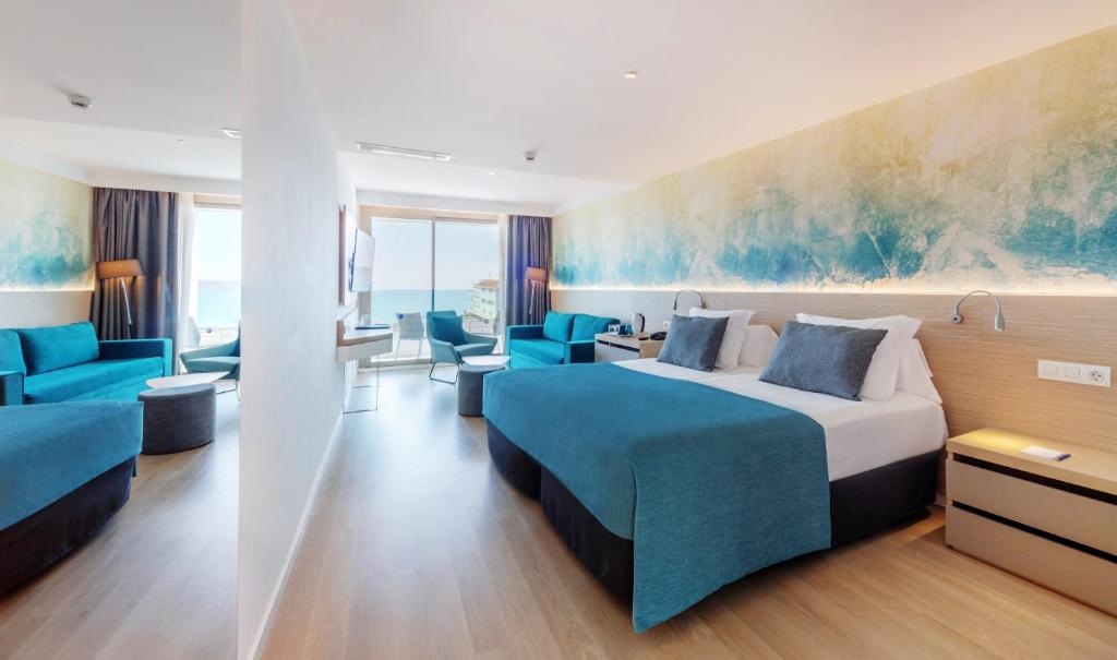 Mūsdienīgs viesnīcas numurs ar skaistu skatu uz jūru, iekārtots ar stilīgām mēbelēm un gaišām krāsām. Telpā ir gulta, atpūtas zonas un liels logs, nodrošinot dabīgu apgaismojumu.