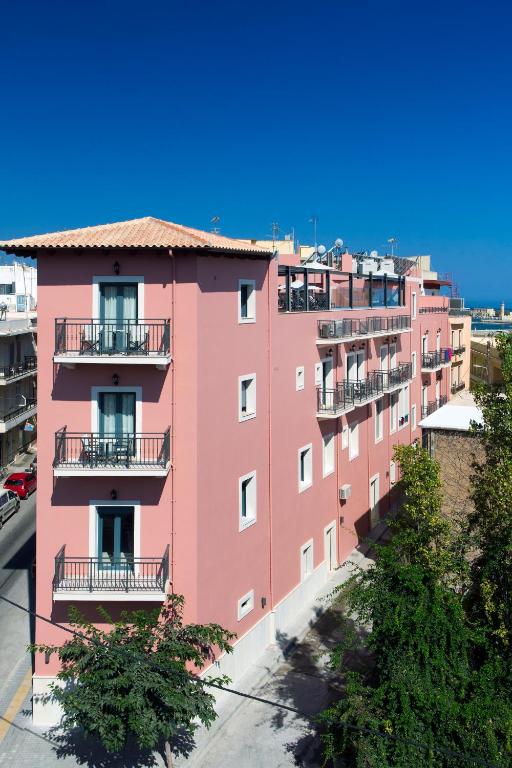 Rozā ēka ar balkoniem un skatu uz zilu debesu, blakus ielai un kokiem. Ideāla vieta, lai izbaudītu pilsētas atmosfēru.