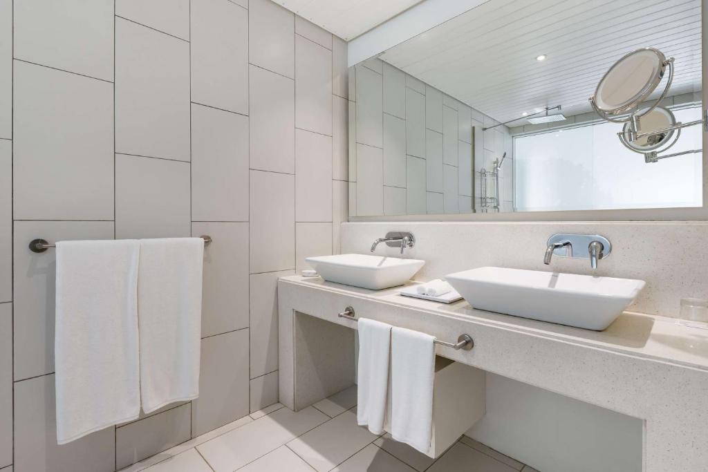 Moderns vannas istabas interjers ar divām izlietnēm, baltiem dvieļiem un spoguli. Gaišas flīzes un minimālistisks dizains rada svaigu atmosfēru.