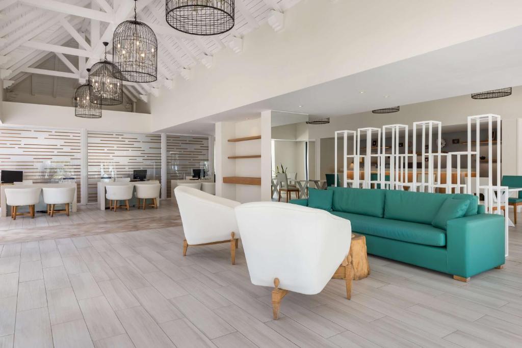 Mūsdienīgs un gaišs interjers ar zaļu dīvānu un baltām krēsliem, kas rada viesmīlīgu atmosfēru. Telpā ir redzami elegantie lampas un darba vietas, nodrošinot komfortu un stilu.