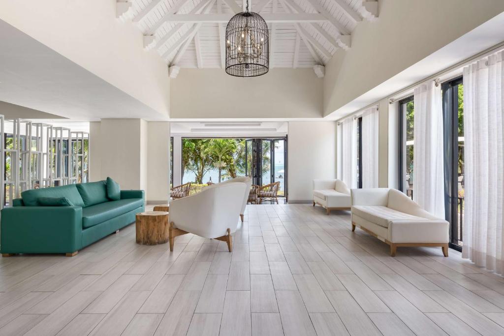 Mūsdienīgs un gaišs viesnīcas interjers ar zaļu dīvānu, baltām mēbelēm un lieliem logiem, caur kuriem redzams dārzs. Piemērots relaksācijai un atpūtai.