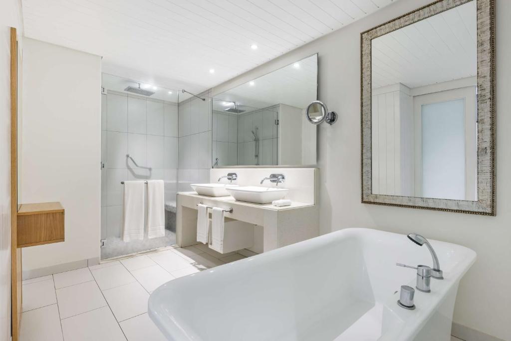 Mūsdienīgs vannas istabas interjers ar divām izlietnēm, stikla dušu un brīvi stāvošu vannu. Eleganta spoguļa un koka elementu kombinācija rada stilīgu un funkcionālu telpu.