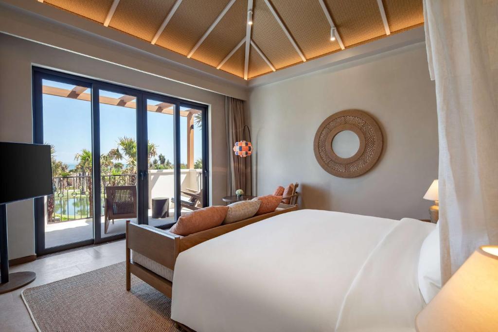 Mūsdienīga viesnīcas numura interjers ar plašiem logiem, kas sniedz skatu uz terasi un ārpusi. Telpā ir ērta gulta, moderns mēbeļu dizains un silta apgaismojuma atmosfēra.