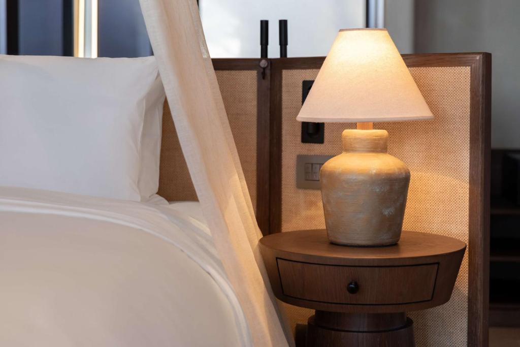 Mūsdienīgs guļamistabas interjers ar gultu un elegantu lampu uz naktsgaldiņa. Gaisma no lampas rada siltu un mājīgu atmosfēru.