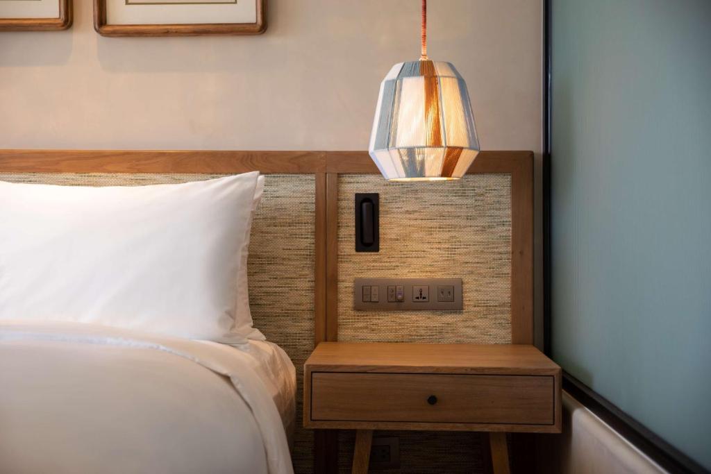 Mūsdienīga guļamistaba ar koka gultas galvgali un naktsgaldiņu, uz kura atrodas lampiņa ar ģeometrisku dizainu. Svaiga un eleganta atmosfēra.