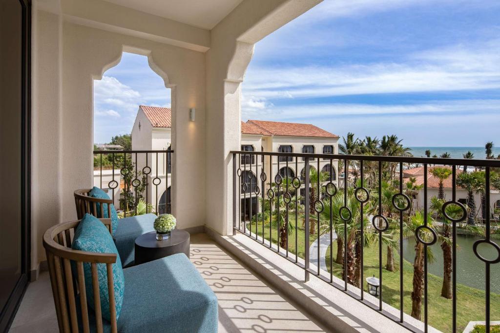 Balconā redzama mūsdienīga sēdvieta ar skatu uz dārzu un jūru. Telpa ir gaiša, ar dekoratīvu metāla margu un palmām.