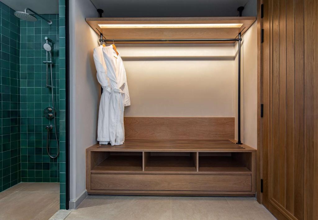 Mūsdienīgs un elegants vannas istabas interjers ar zaļām flīzēm, koka soliņu un baltu halātu pakarinātu uz stieples. Ideāls relaksācijas un komforta stūris.