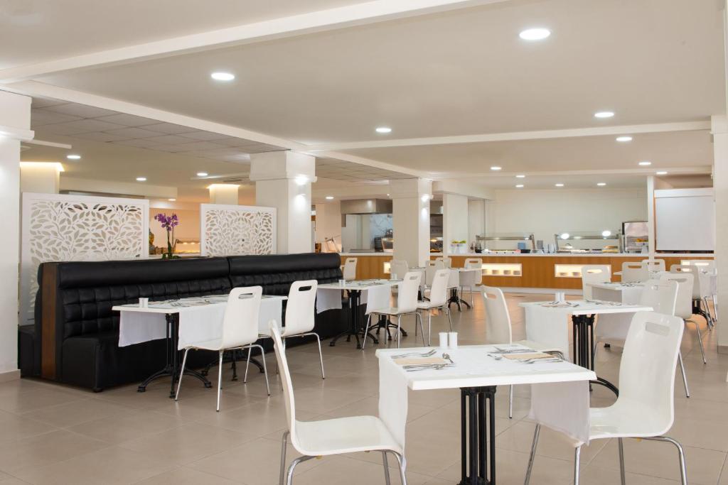 Moderns restorāns ar gaišu interjeru, baltām galdautām un melnu dīvānu, kas nodrošina ērtu sēdēšanu. Ziedu dekorācijas un atvērtā virtuve rada patīkamu atmosfēru.