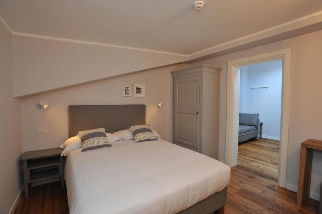 Mūsdienīga guļamistaba ar divguļamo gultu, koka grīdu un gaišiem sienām, kas rada mājīgu atmosfēru. Telpā redzama arī skapja un dīvāna zona.