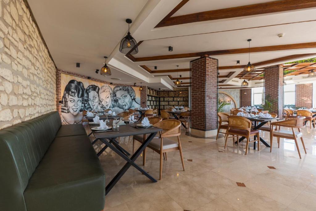 Moderns restorāns ar stilīgu interjeru, kas ietver mākslinieciski noformētu sienu un eleganti sakārtotas galdiņas. Gaisīga atmosfēra un dabīgi elementi rada aicinājumu apmeklēt.