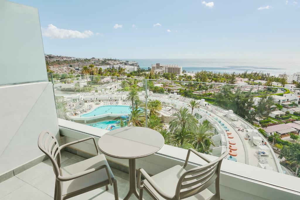 Skats no balkona uz viesnīcas teritoriju ar baseinu un jūru fona. Palmām un citiem zaļumiem apkārt, kas veido mierīgu un relaksējošu atmosfēru.