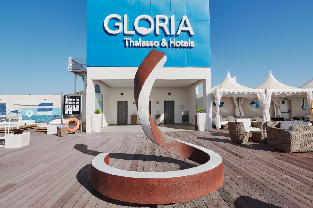 Gloria Thalasso & Hotels zīme ar mūsdienīgu skulptūru viesnīcas terasē, kas piedāvā relaksējošu atmosfēru un komfortablu atpūtu.