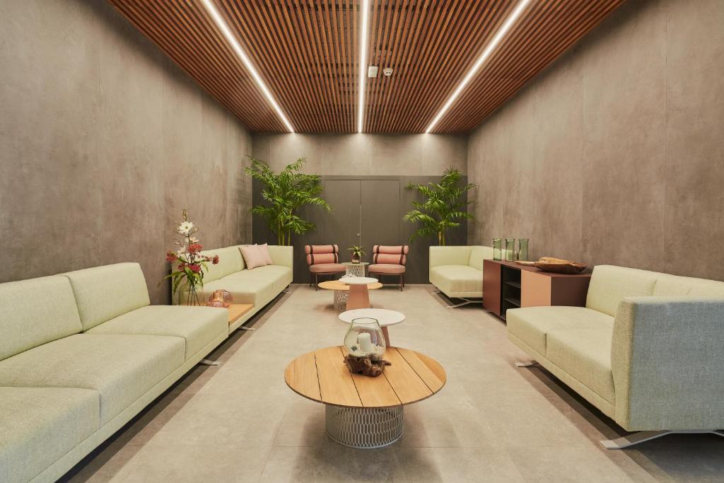 Mūsdienīgs un stilīgs interjers ar gaišām dīvānu zonām, koka griestiem un augiem, radot relaksējošu atmosfēru. Centrā atrodas apaļš koka galds.