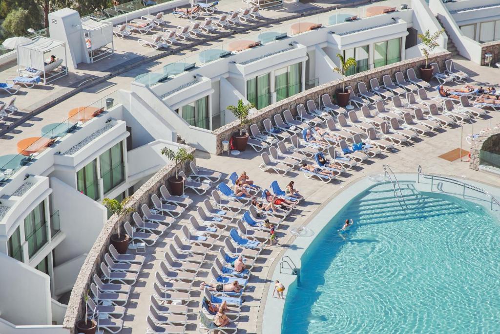 Peldbaseins ar saules krēsliem un viesiem, kas atpūšas pludmales atmosfērā. Modernā viesnīcas terase ar skatu uz ūdeni.