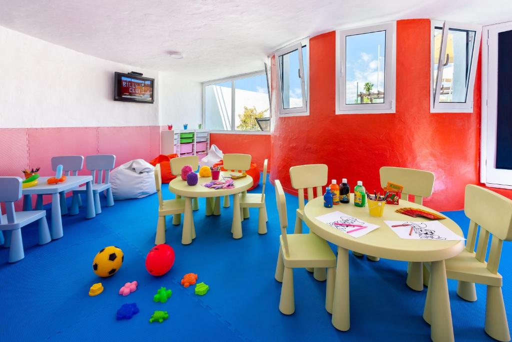 Krāsaina bērnu istaba ar rotaļām un galdiem, kur bērni var zīmēt un spēlēt. Telpā ir spilgti krāsoti krēsli, dažādas spēles un rotaļlietas.