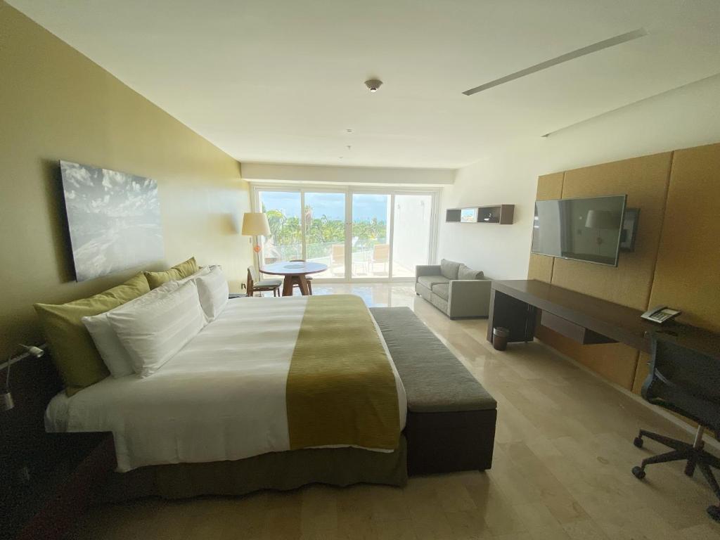 Mūsdienīga viesnīcas numura interjers ar plašu gultu, dīvānu un galdu, kas piedāvā skatu uz dārzu. Numurā ir televizors un darba zona.