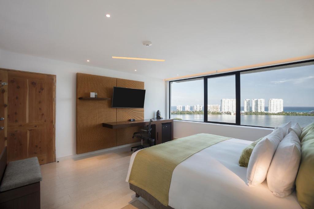 Mūsdienīga guļamistaba ar plašu logu, no kura paveras skats uz pilsētu un jūru. Telpā ir ērts gultas veļas komplekts un televizors, radot komfortablu atmosfēru.