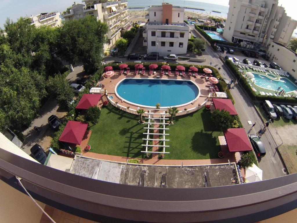 Baseins ar saulessargiem un zālienu, redzams viesnīcas komplekss un tuvā pludmale.