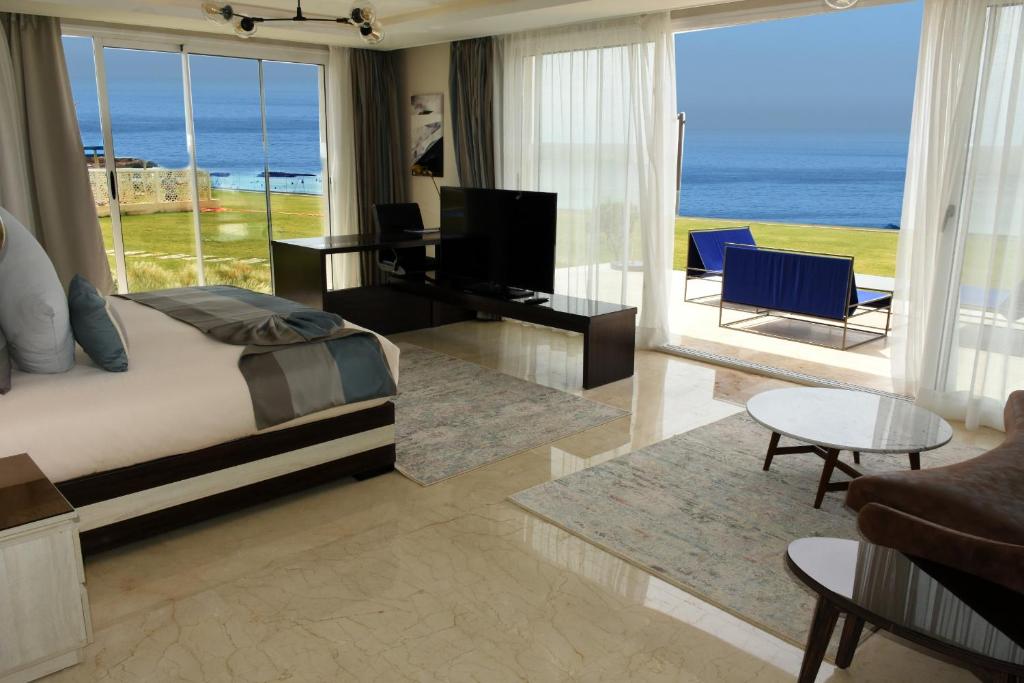 Mūsdienīgs viesnīcas numurs ar skatu uz jūru, gaišiem interjera elementiem un ērtu mēbelējumu. Logi nodrošina lielisku dabiskā apgaismojuma plūsmu un pieeju ārējai terasei.