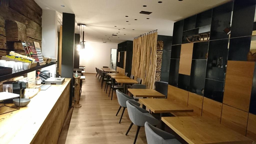 Mūsdienīgs restorāna interjers ar koka mēbelēm un siltām krāsām, kas rada patīkamu atmosfēru. Redzama kafejnīcas lete un ēdamgaldi, kas gaida apmeklētājus.