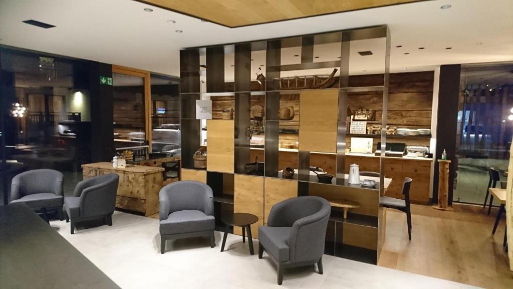 Mūsdienīgs interjers ar ērtām pelēkām krēsliem un koka elementiem, kas rada siltu atmosfēru. Redzama recepcija un dekoratīvi elementi, kas papildina telpas estētiku.